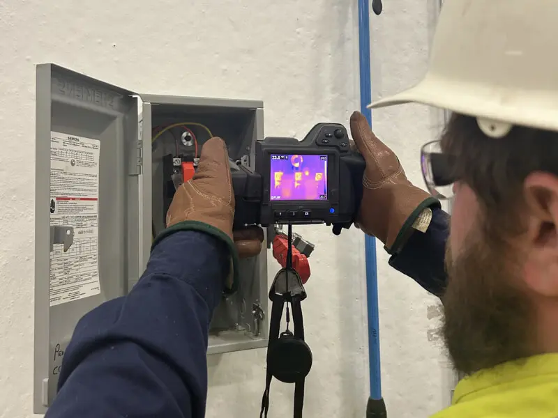 Man in hard hat using infrared scanner to test electrical panel